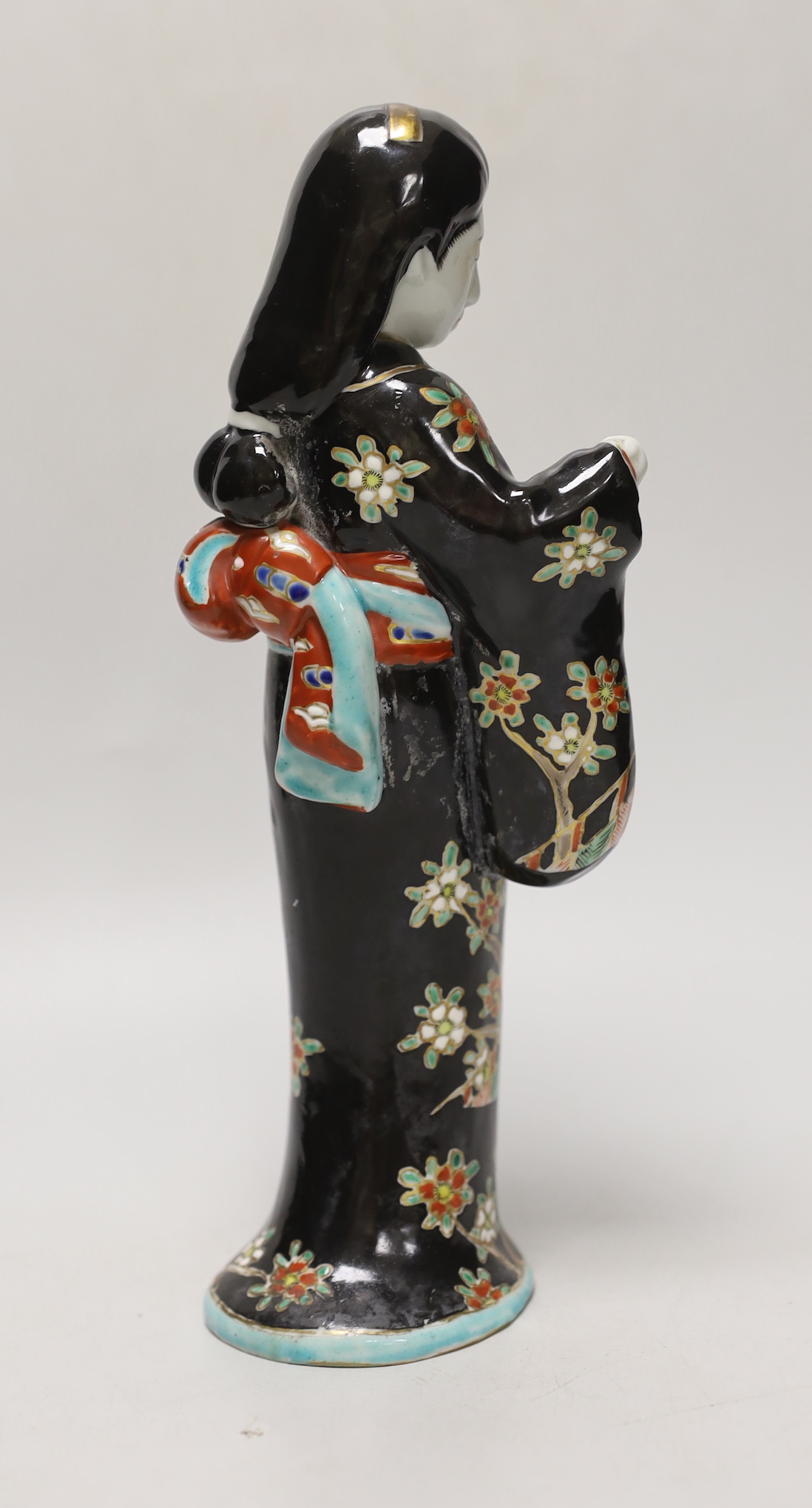 A Japanese porcelain figure of a geisha girl wearing a floral blue ground kimono, 27cm tall